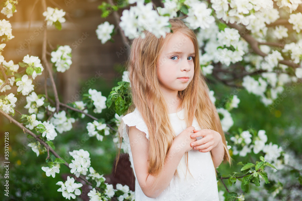 Fototapeta premium Beautiful preteen girl with long blond hair enjoy spring apple blooming. Little preschool girl in garden tree flowers. Copy space for text.