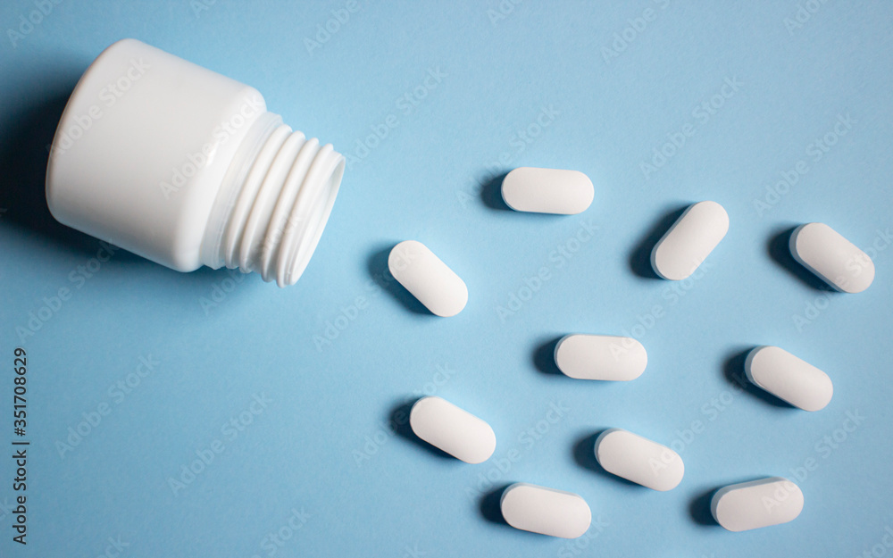 White medical pills and tablets spilling out of a medical bottle. Macro top down view. Blue background.