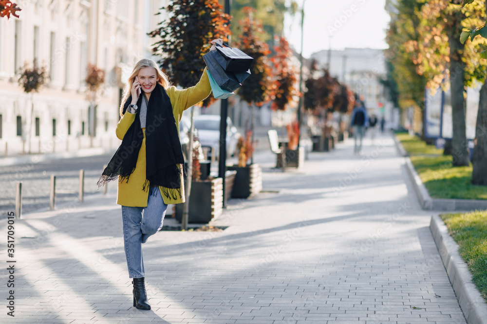 cute attractive blonde woman with packages on the street in sunny weather. communicates on the phone after shopping, positive emotions. cute attractive blonde woman with packages on the street in sunny weather. communicates on the phone after shopping, positive emotions.