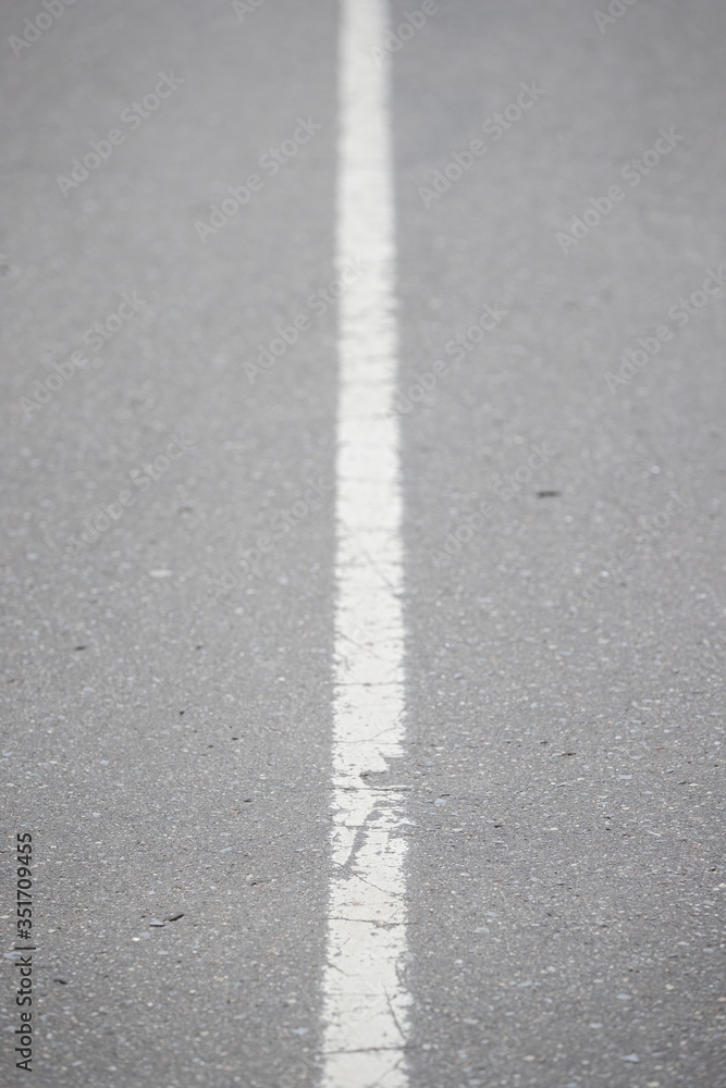 White continuous line on asphalt. Road marking on the highway. Selective focus of the line stretching into the distance. A line dividing the road into two parts.