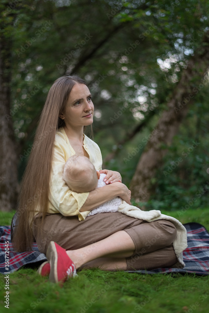 Young beautiful mother holding baby and sitting on picnic blanket. Vertical frame Young beautiful mother holding baby and sitting on picnic blanket. Vertical frame