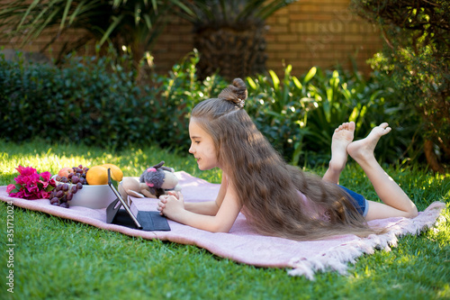 Little girl, schoolgirl looks in a laptop in the garden