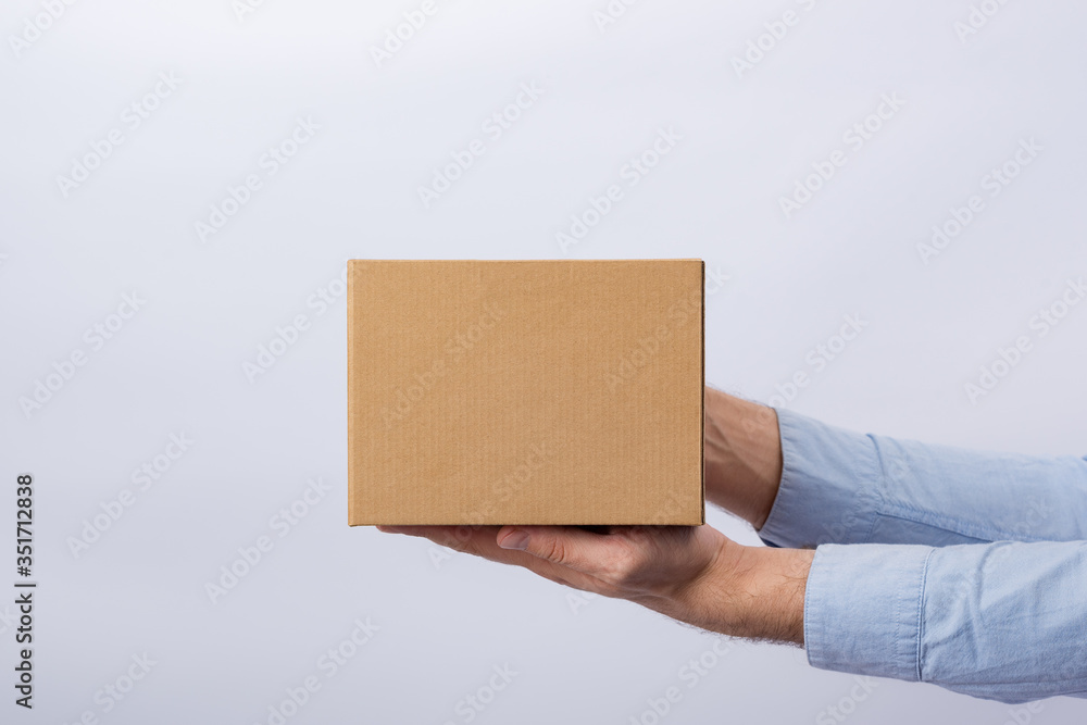 Man holding box at arm's length. White background. Square cardboard box. Delivery of parcels. Side view. Man holding box at arm's length. White background. Square cardboard box. Delivery of parcels. Side view.