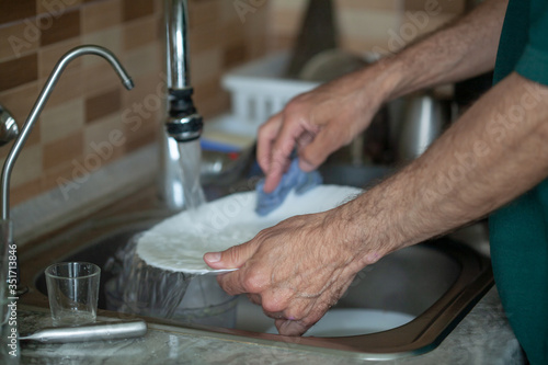 Fotografie Men housework washes dishes in the sink, a dirty pan and plates under running water, the husband helps with the housework during quarantine of the coronavirus