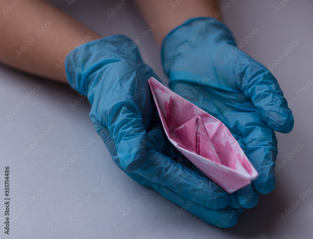 Hands in gloves holding origami a boat from the pink paper. Concept for a travel after the end of quarantine. New life after Pandemic COVID-19 concept.