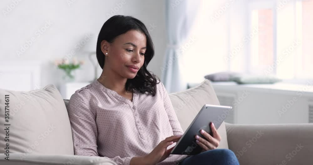 Beautiful young african american woman sitting om comfortable sofa, using digital computer tablet at home. Relaxed mixed race businesswoman web surfing information online, working alone from home. Beautiful young african american woman sitting om comfortable sofa, using digital computer tablet at home. Relaxed mixed race businesswoman web surfing information online, working alone from home.