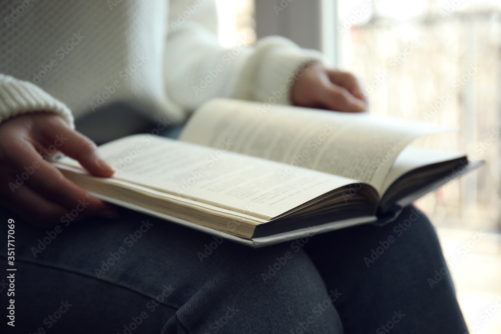 Woman reading book near window indoors, closeup Woman reading book near window indoors, closeup