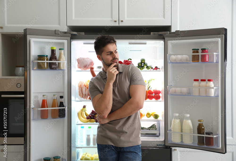 Thoughtful young man near open refrigerator in kitchen Thoughtful young man near open refrigerator in kitchen