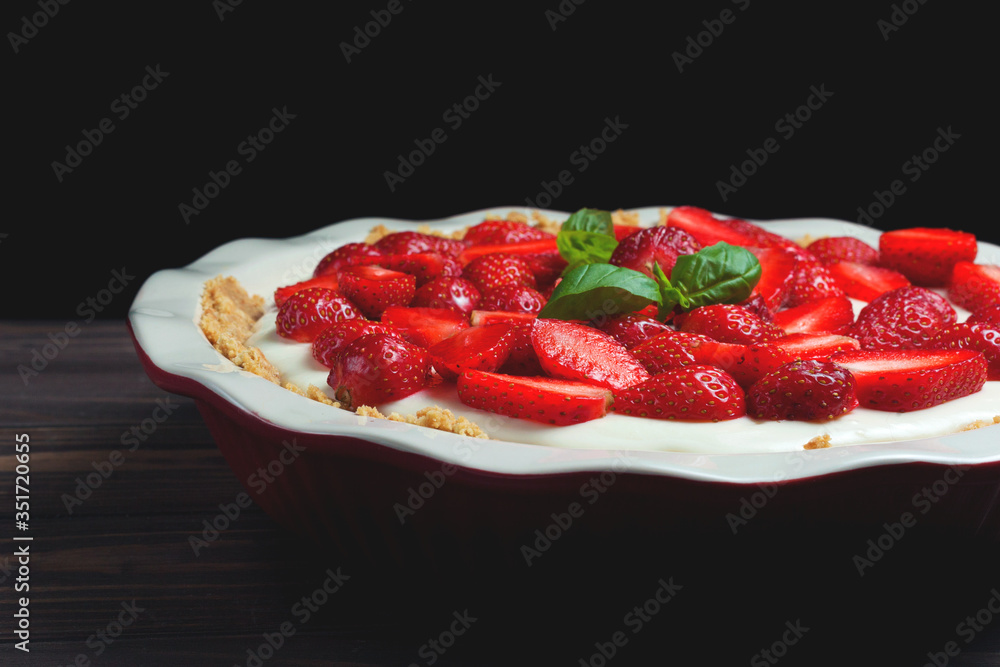 Strawberry cheesecake with basil leaves, in a red ceramic baking dish on a wooden background Strawberry cheesecake with basil leaves, in a red ceramic baking dish on a wooden background