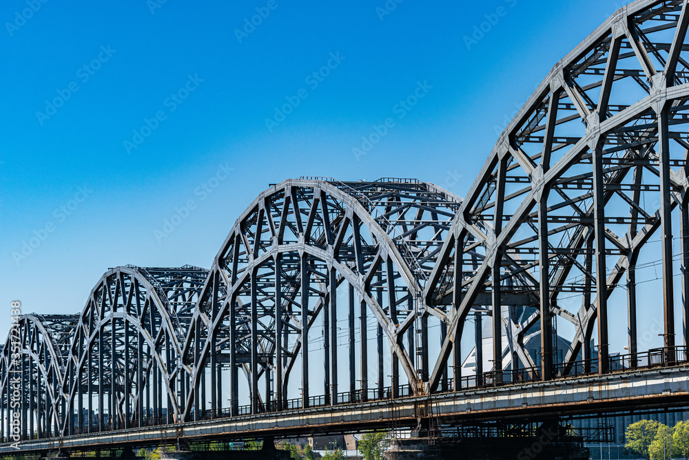 Large gray steel railway bridge against blue sky in sunny day. Riga, Latvia Large gray steel railway bridge against blue sky in sunny day. Riga, Latvia