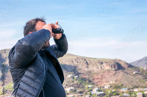 Close up of a man looking through binoculars, outdoors.