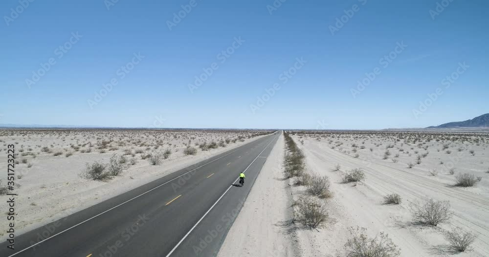 Cyclist riding along long straight road, surrounded by desert and sand Cyclist riding along long straight road, surrounded by desert and sand