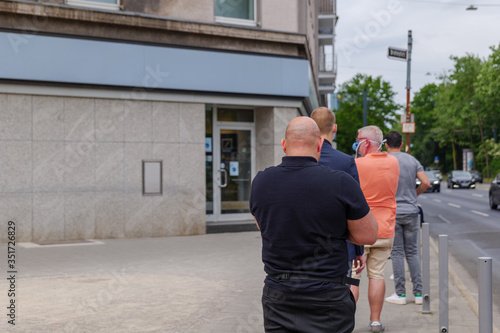 Selected focus view, Group of European men with wearing face mask queue and wait for get in a bank on sidewalk during social distancing and quarantine regulations for COVID-19 virus. © Peeradontax