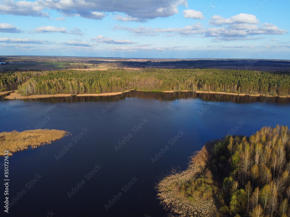 Aerial shot of storage reservoir. Landscape with blue sky and white clouds, flat terrain, river, forest, top view.