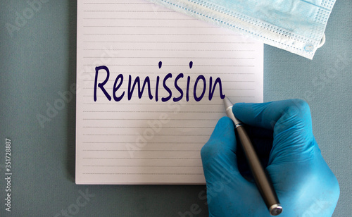 Photos Male doctors hand in blue glove writes the word 'remission' on a white note