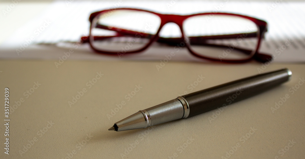 Fototapeta premium Metal pen and beautiful glasses on a white table. Business concept.