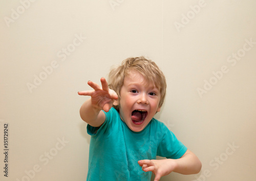 little boy with blond hair threw forward his right hand, posing on a gray background