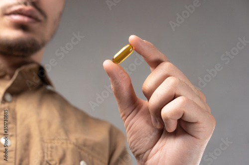 A man holds a pill (fish oil capsule) in his hand on a gray background