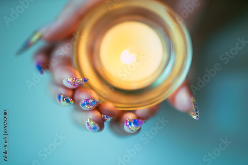 Female hands with sharp nails holding a candlestick with a burning candle