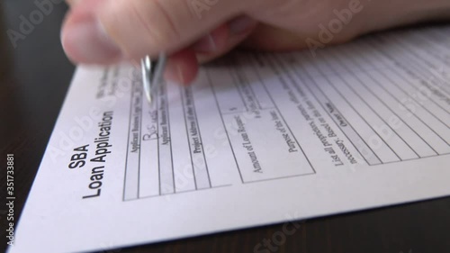 A Small Business Administration aka SBA loan application form, issued by the U.S.A. government, is shown up close being filled out by a male hand with an ink pen. photo