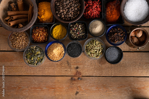 Different kinds of bowls with spices on a wooden surface