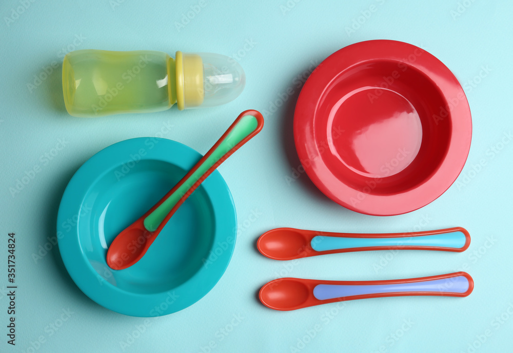Set of colorful plastic dishware on light blue background, flat lay. Serving baby food - obrazy, fototapety, plakaty 
