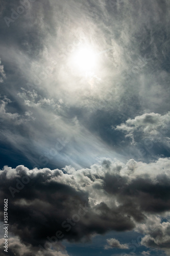 dramatic stormy sky with a blurred sun disk and heavy cumulus clouds against a dense cloud cover. artwork picture for fantasy, abstract or moody design or decoration