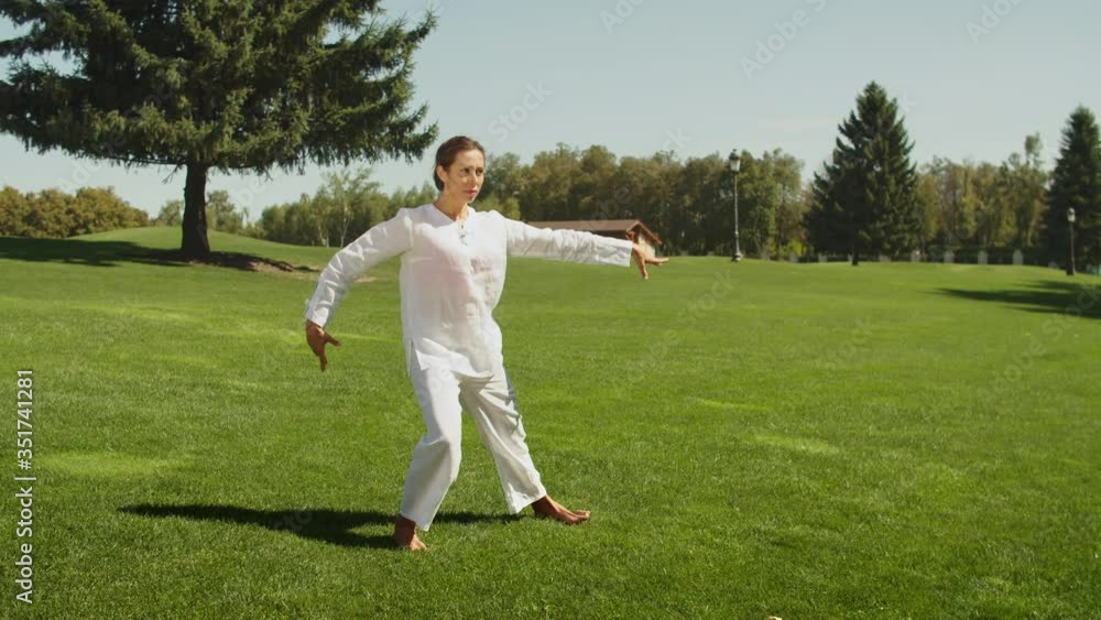 Woman in white suite performing yoga-asanason the grass. Young attractive slim girl in bodysuit relaxing and doing exercises. Woman in white suite performing yoga-asanason the grass. Young attractive slim girl in bodysuit relaxing and doing exercises.