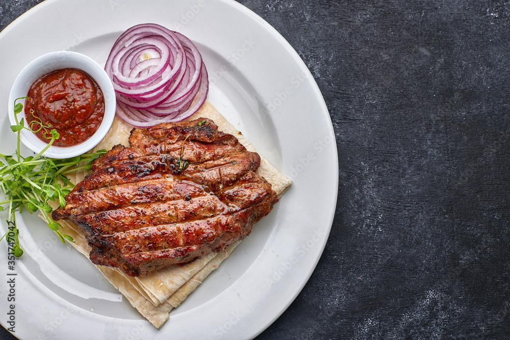 Grilled meat steak with onions, sauce and microgreen, on pita bread, on a white plate, against a dark background. space for text. top view