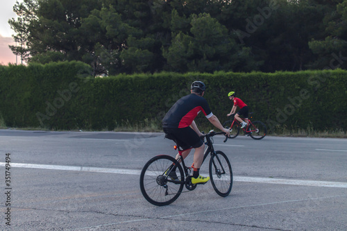 Cyclists ride, dressed up with red and black cloths on country roads on a evening in Spain.