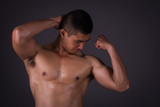 Muscular model Asian young man on Gray background. Portrait of strong brutal guy with trendy hairstyle. Sexy naked torso, six pack abs. Male flexing his muscles. Sport workout bodybuilding concept.