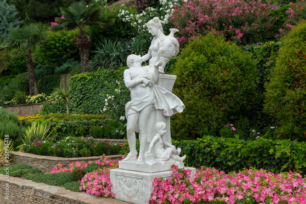 Alushta, Russia - July 29, 2016: Statue of a couple in love in the Aivazovsky landscape park in Partenit in the Crimea against the backdrop of evergreen and flowering shrubs.