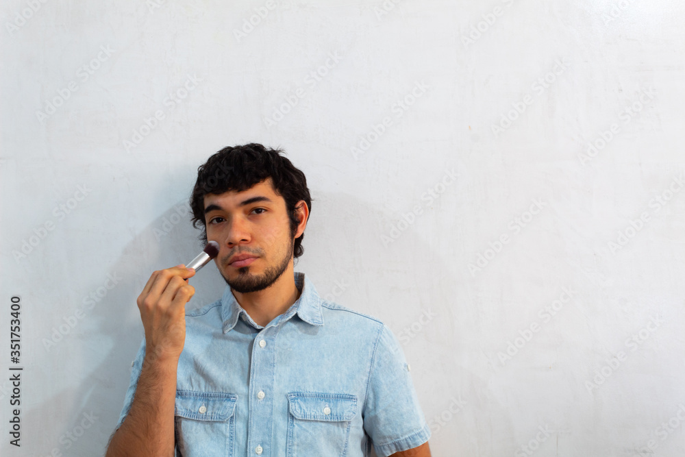 Non-binary bearded young Hispanic man on a white background posing with a makeup brush Non-binary bearded young Hispanic man on a white background posing with a makeup brush