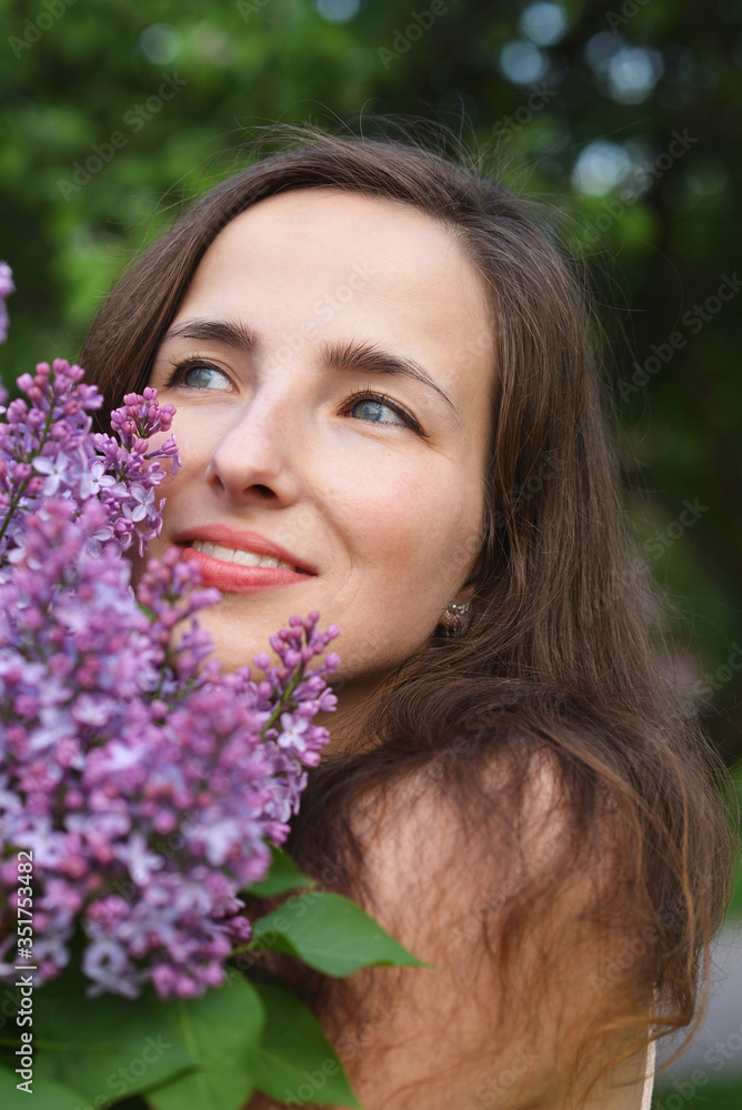 The face of a happy smiling young beautiful girl with a Bush of blooming lilac The face of a happy smiling young beautiful girl with a Bush of blooming lilac