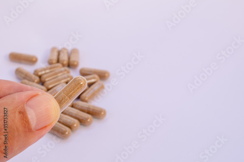 fingers holding herbal capsule, nutritional supplement, vitamin pill, herbal medicine on white background. Tribullus Terrestris