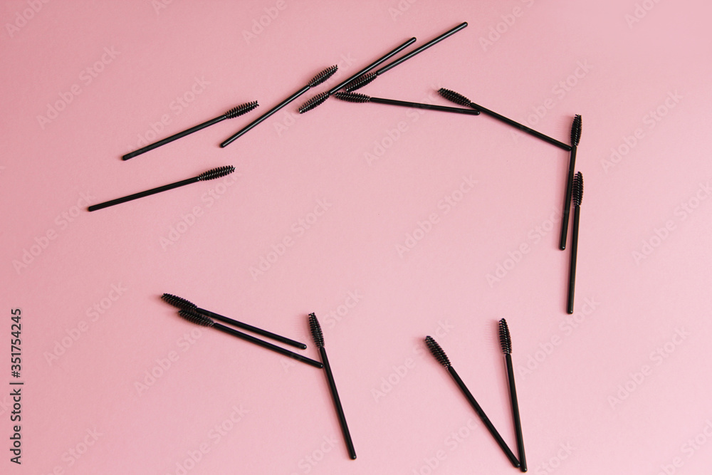 a lot of black mascara brushes on a pink background are scattered carelessly