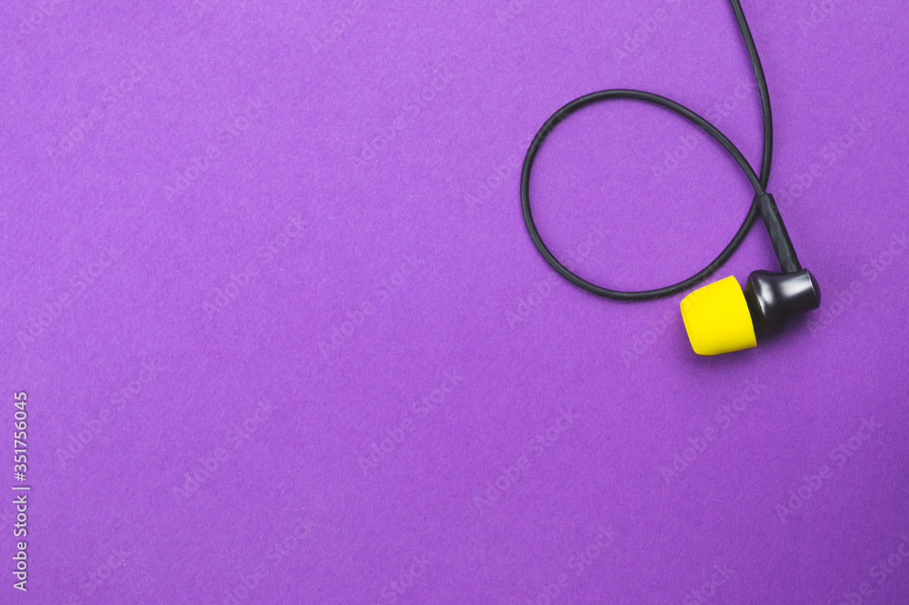 Earphone with yellow ear cushion on a purple background. in-ear headphones. modern style. audio equipment Earphone with yellow ear cushion on a purple background. in-ear headphones. modern style. audio equipment