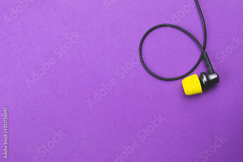 Earphone with yellow ear cushion on a purple background. in-ear headphones. modern style. audio equipment