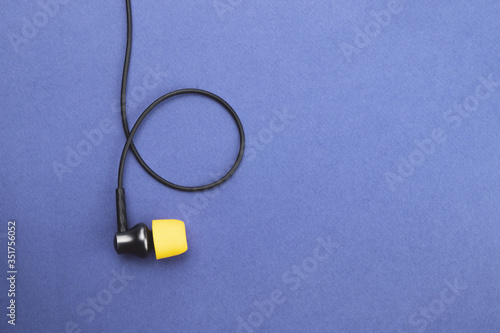Earphone with yellow ear cushion on a blue background. in-ear headphones. audio equipment