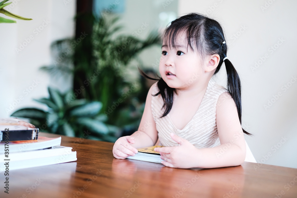 Cute asian girl learning by reading and studying books and playing at home in the living room sitting, home schooling education for children, feeling happy cheerful, and enjoying staying at home