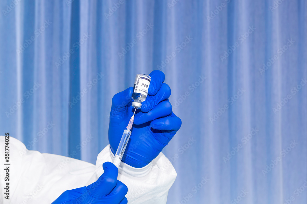 Medical researcher uses syringe to get example of vaccine from the bottle. Scientist in PPE suit works in laboratory room testing vaccine for pandemic prevention. COVID-19 vaccine is under experiment. Medical researcher uses syringe to get example of vaccine from the bottle. Scientist in PPE suit works in laboratory room testing vaccine for pandemic prevention. COVID-19 vaccine is under experiment.