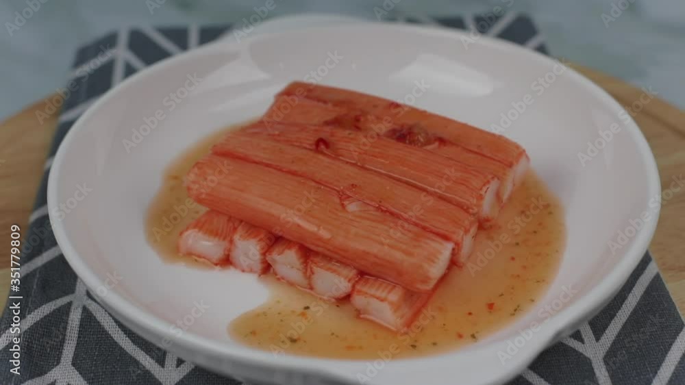 Pouring Thai spicy seafood sauce on top of Crab sticks from fish protein ( surimi ) imitation crabmeat on a white plate , rotating Pouring Thai spicy seafood sauce on top of Crab sticks from fish protein ( surimi ) imitation crabmeat on a white plate , rotating