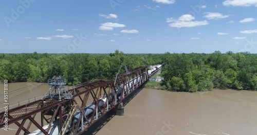 Tracking cargo train finishing crossing large river into dense forest 