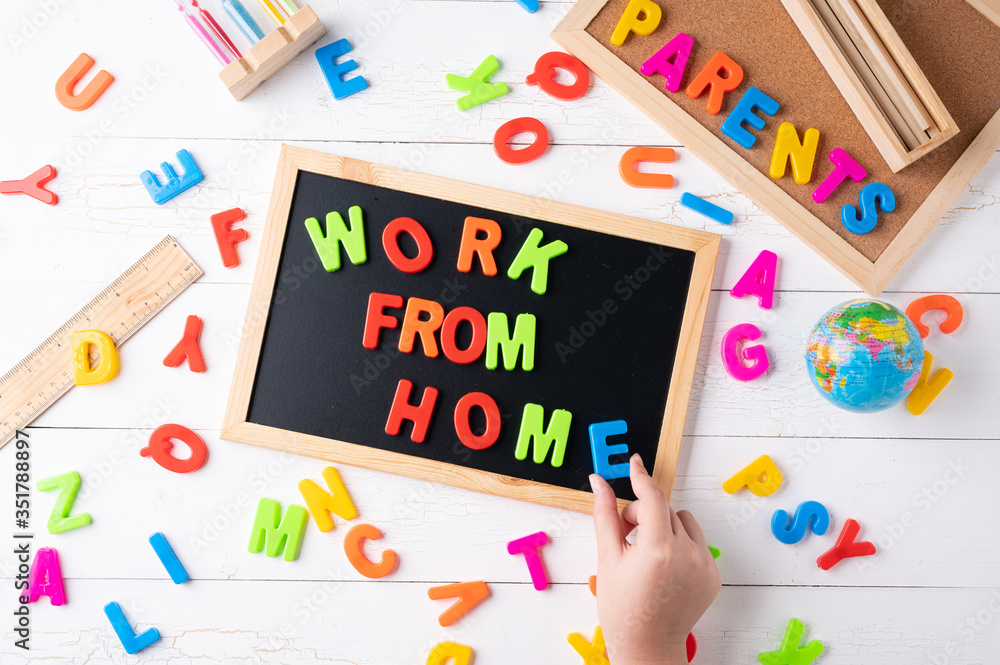 `Work from Home` words on a modern board on a white wooden surface, top view. Overhead, from above, flat lay. `Work from Home` words on a modern board on a white wooden surface, top view. Overhead, from above, flat lay.
