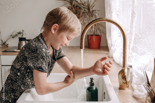 Photo of a fair-haired boy of European appearance. 7-year-old child washes his hands over the sink in front of the window. Viral Prevention in Infectious Diseases
