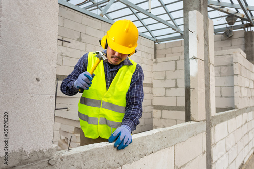 Construction workers use a hammer to hammer a concrete nail into a lightweight concrete block to build a house..