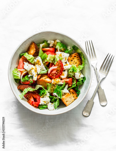 Simple salad with fresh tomatoes, crispy ciabatta, mozzarella cheese, green salad with olive oil, mustard, lemon dressing on a light background, top view