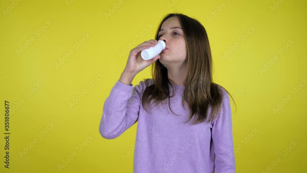 Teen girl in a pink sweater drinks yogurt with a white plastic bottle