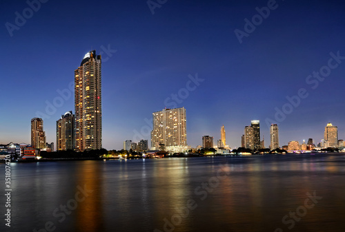 Golden blue sky at Chao Phraya River with lighting on the building in cityscape.