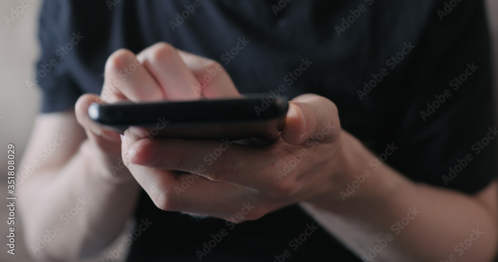Closeup young man in black t-shirt use smartphone while sitting on a couch